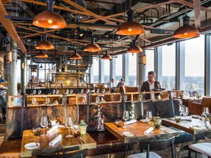 Een restaurant met verschillende eettafels, hangende koperen吊り下げランプ en uitzicht over de stad.