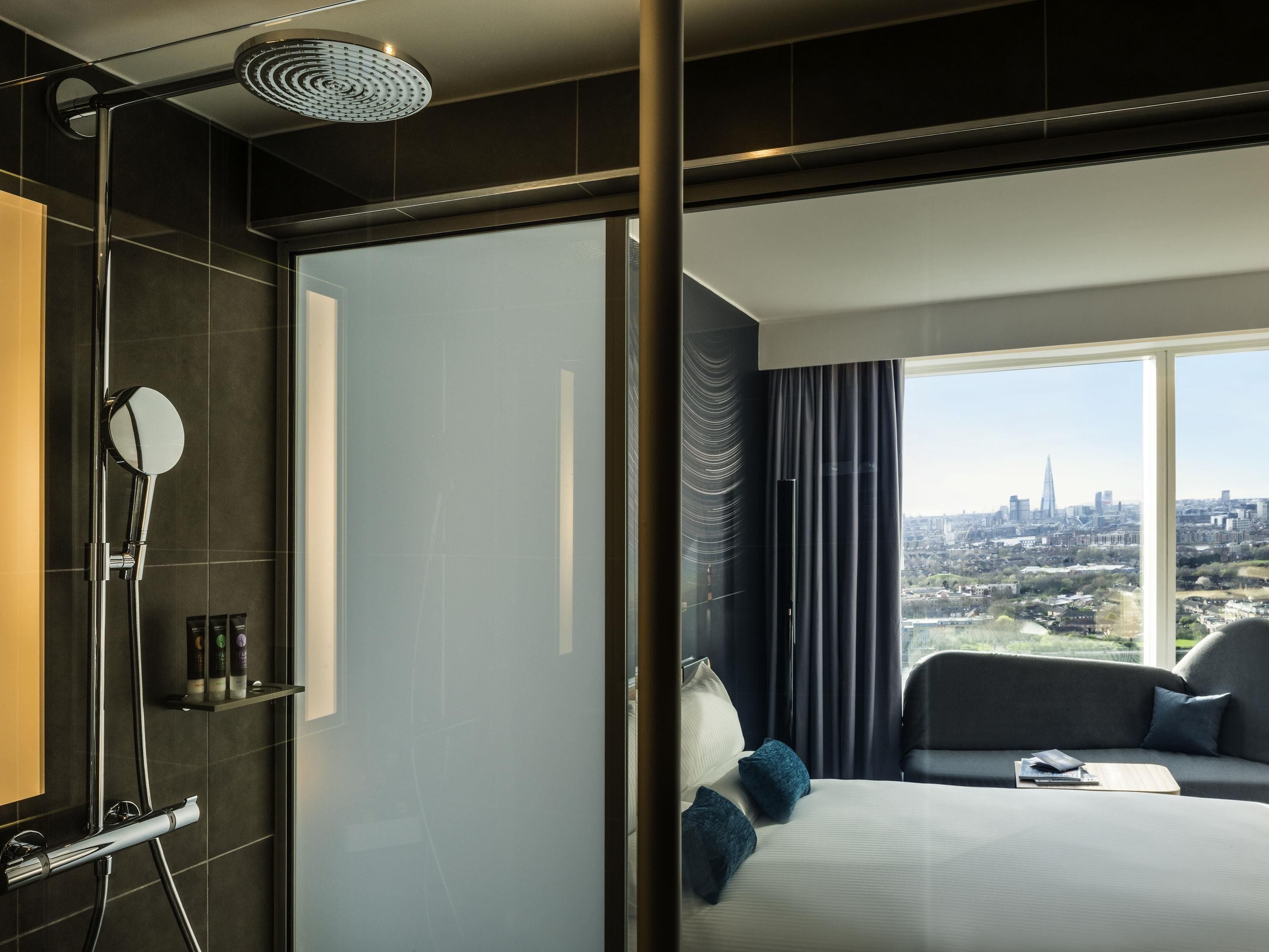 Habitació d'hotel moderna amb una finestra gran, un llit, un sofà i una zona de dutxa.