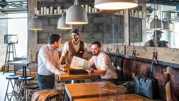 A restaurant interior with wooden tables, bar stools, hanging pendant lights, and a seating area with leather cushions.