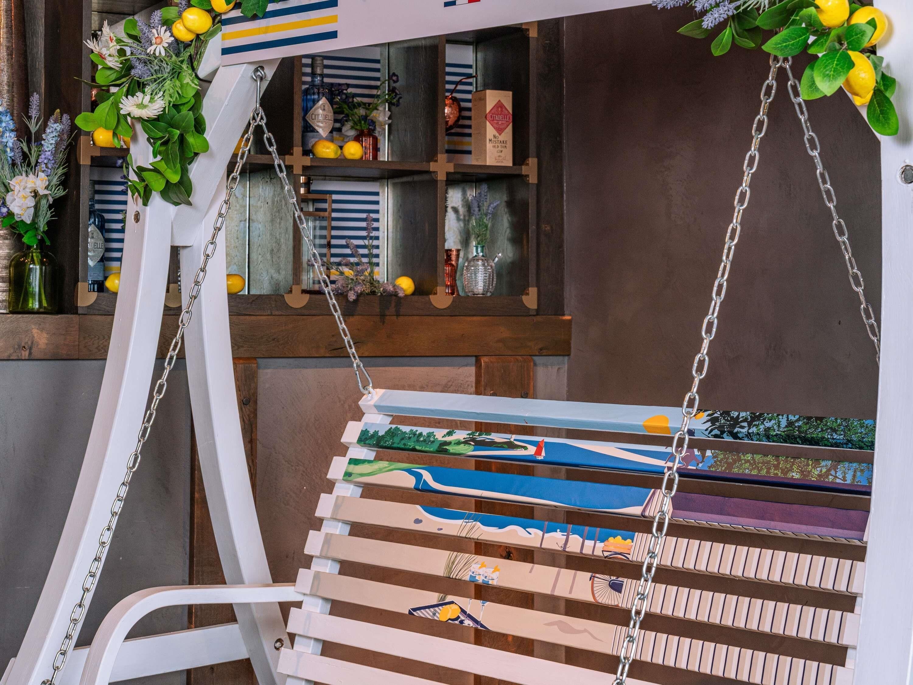 A wooden swing chair with a metal chain, a wall-mounted shelf with various items, and a window with decorative plants.
