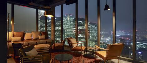 A modern lounge with a city view, featuring a sofa, armchairs, and a round table.