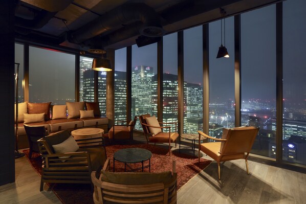 A modern lounge with a city view, featuring a sofa, armchairs, and a round table. - Novotel London Canary Wharf Hotel (London)