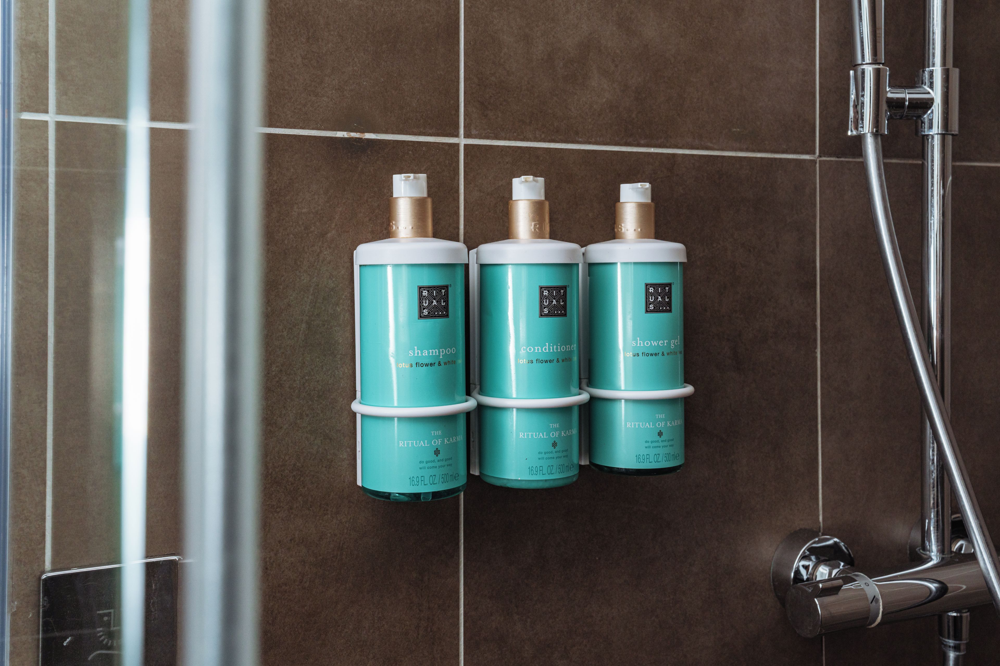 Tres botellas de champú, acondicionador y gel de ducha sobre una pared de azulejos.