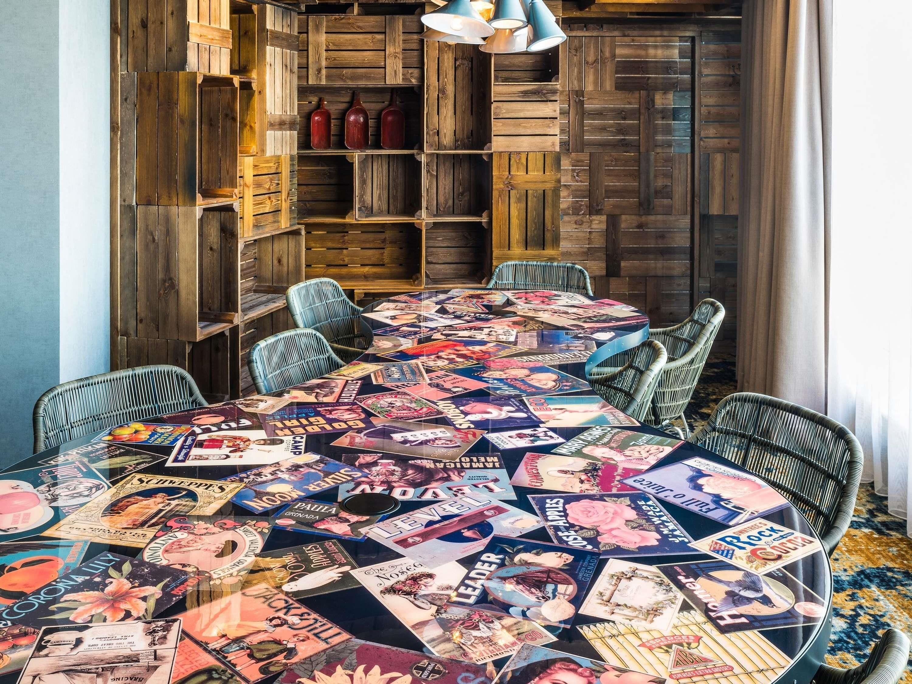A dining area with a table covered in magazines, wicker chairs, and a wooden wall with shelves.