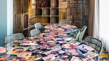 Un coin repas avec une table recouverte de magazines, des chaises en osier et un mur en bois doté d’étagères.