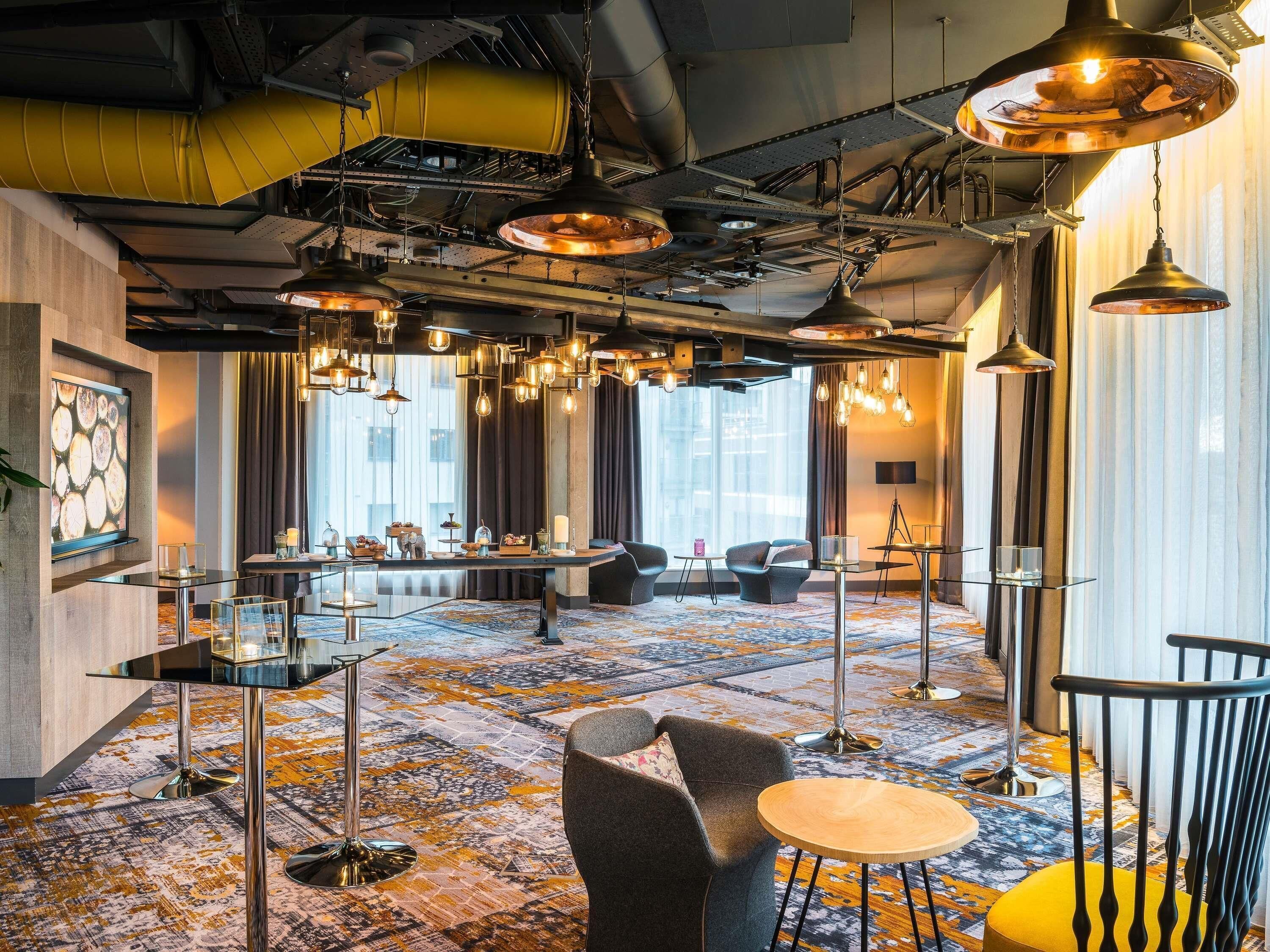 A modern hotel lobby with a patterned carpet, multiple seating areas, and pendant lighting.