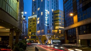 Ein hoch aufragendes Hotel mit einem gut sichtbaren 'NOVOTEL'-Schild, das eine moderne Glasfassade und mehrere Etagen aufweist.