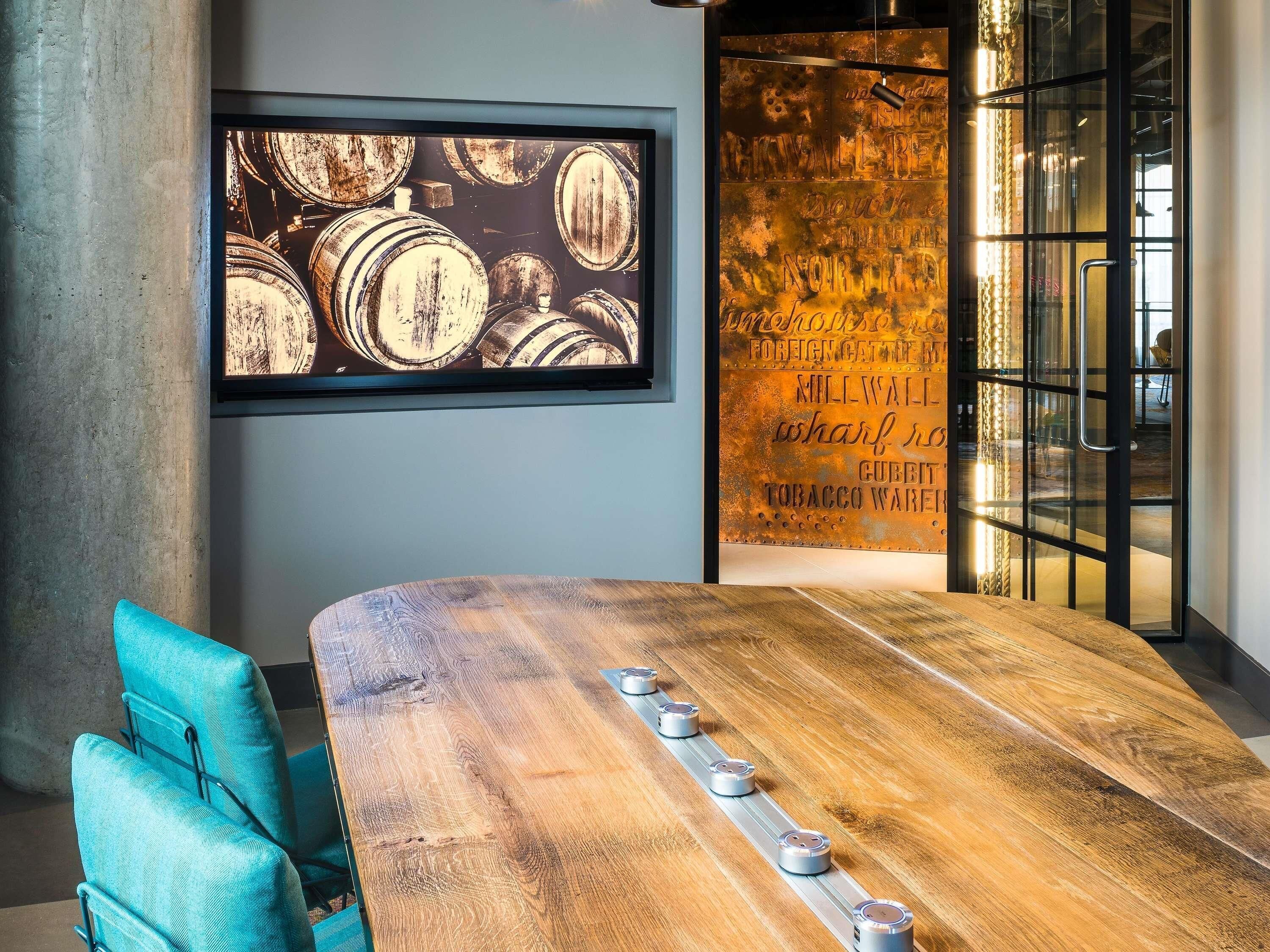 A conference room with a wooden table, teal chairs, a large framed picture of barrels, and a wall with a metal sign.