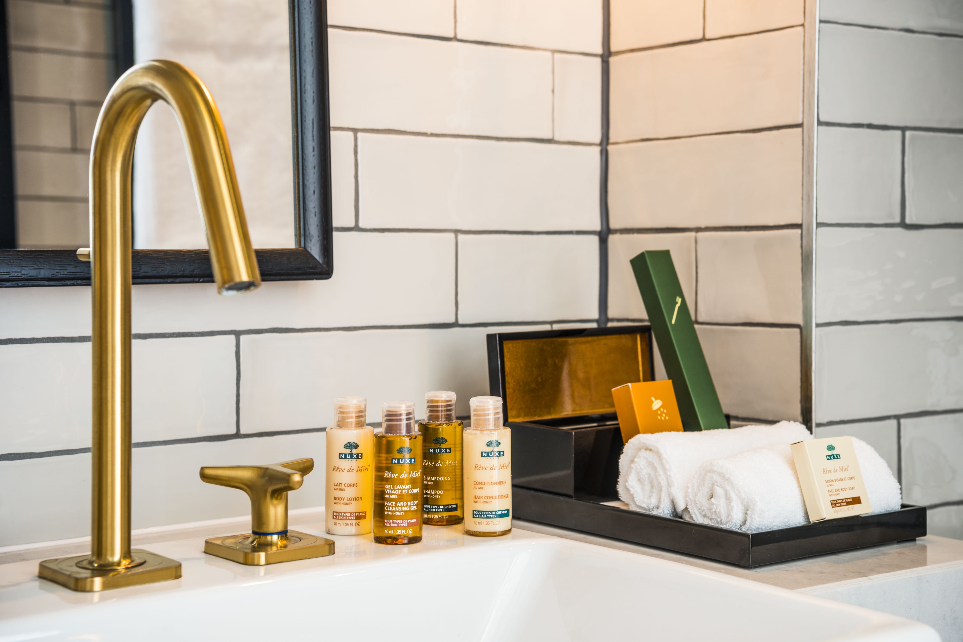 A bathroom with a gold faucet, a black tray holding toiletries, and a mirror with a black frame.
