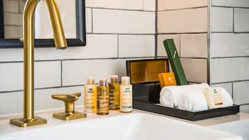 A bathroom with a gold faucet, a black tray holding toiletries, and a mirror with a black frame.