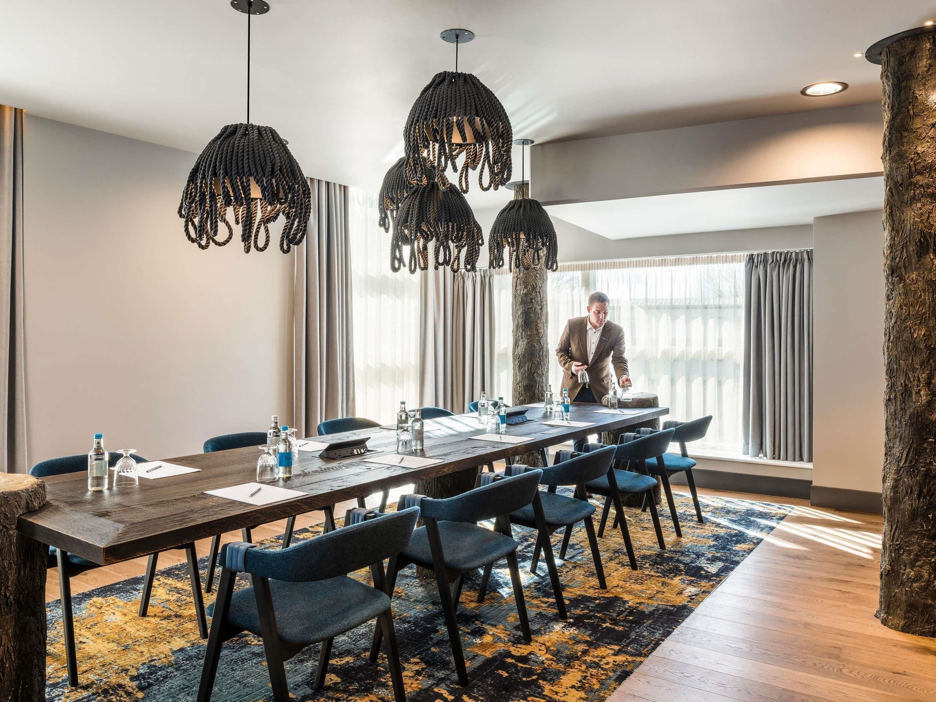 A conference room with a long table, chairs, and hanging pendant lights.