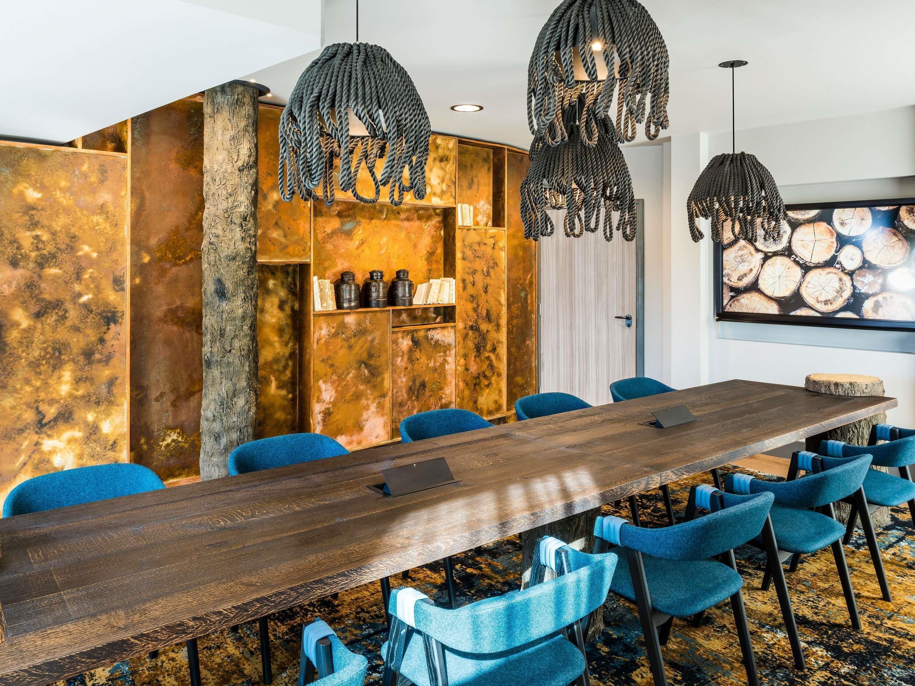 Een congrescentrum met een lange houten tafel, blauwe stoelen en bijzondere touwvloeren.