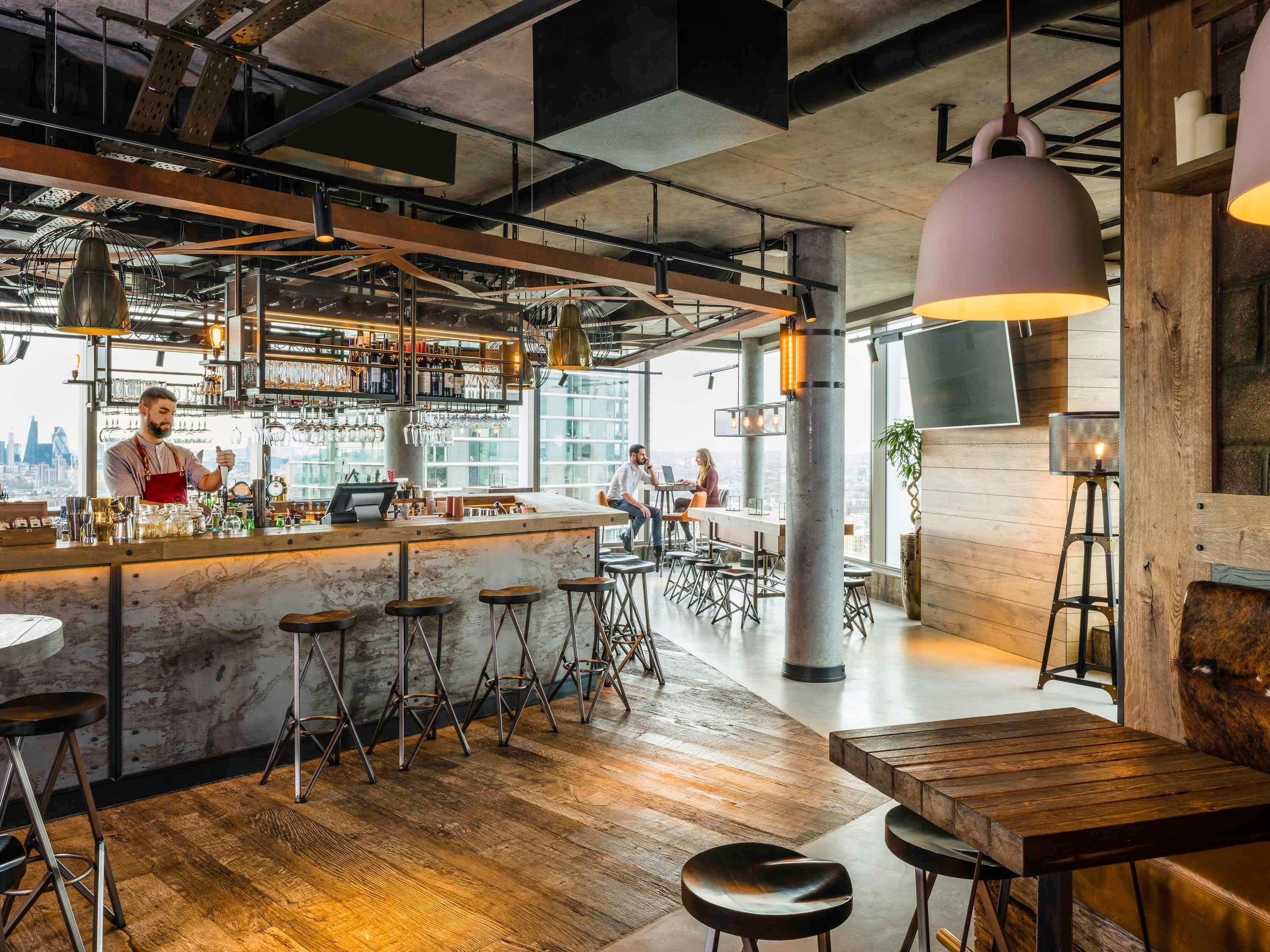 A modern bar area with a bar counter, stools, and hanging pendant lights.