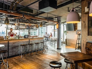 A modern bar area with a bar counter, stools, and hanging pendant lights. - Novotel London Canary Wharf Hotel (London)
