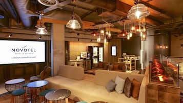 Un hall d’hôtel au design moderne, comprenant un canapé, des tables rondes et des luminaires suspendus.