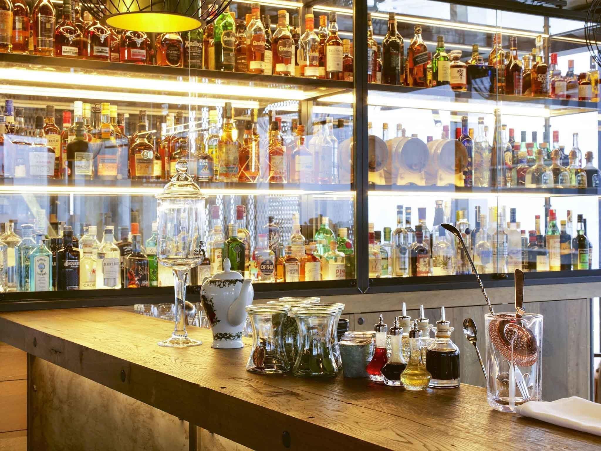 Eine Bar mit Regalen voller Spirituosenflaschen und unterschiedlichem Gläserangebot auf der Theke.