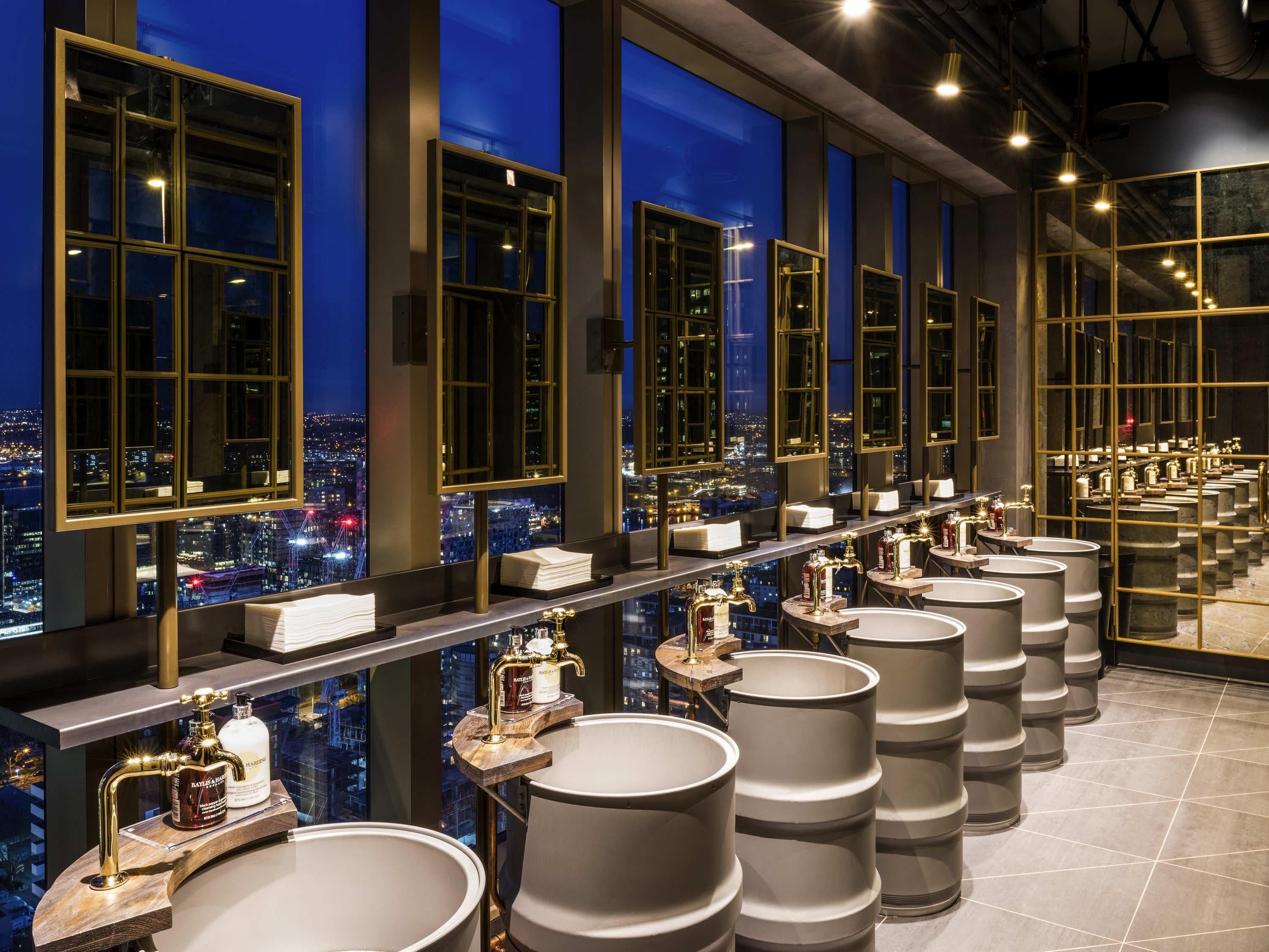 A hotel bathroom with multiple sinks, large mirrors, and a city view.