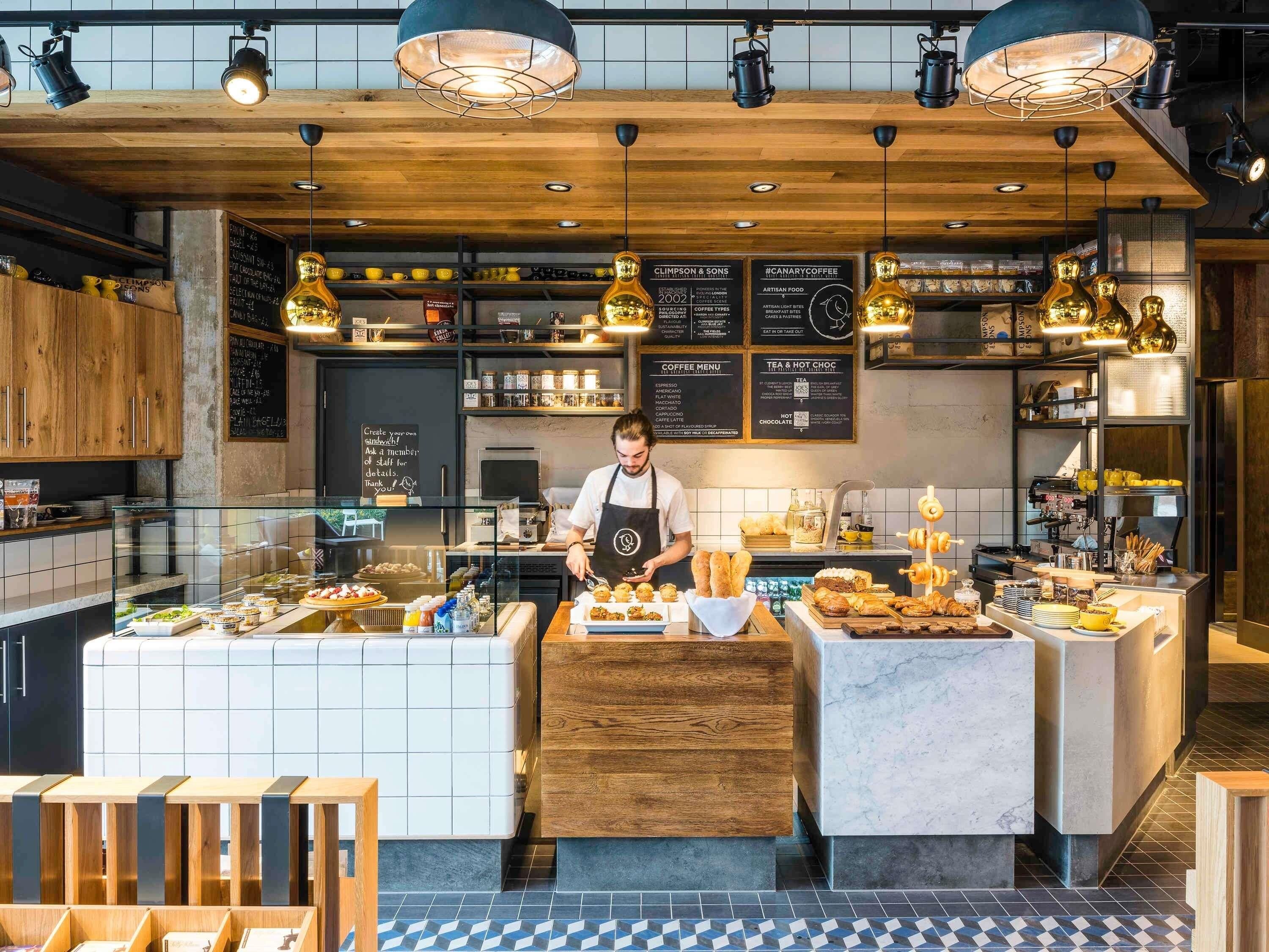 A coffee shop interior with a barista preparing food, a menu board, and various coffee and food items displayed.