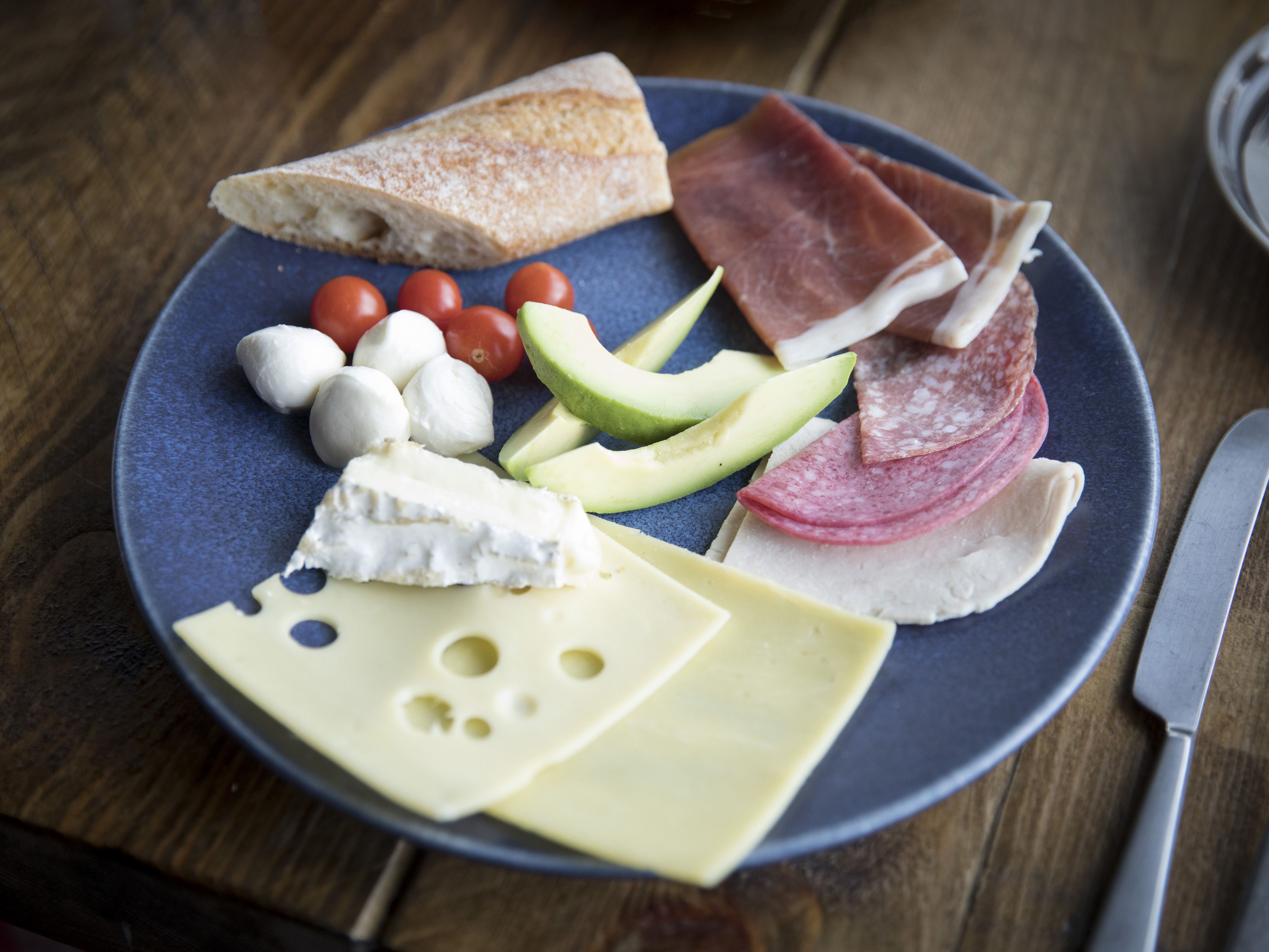 Une assiette garnie de différents fromages, de charcuteries, de tomates et d’avocat.