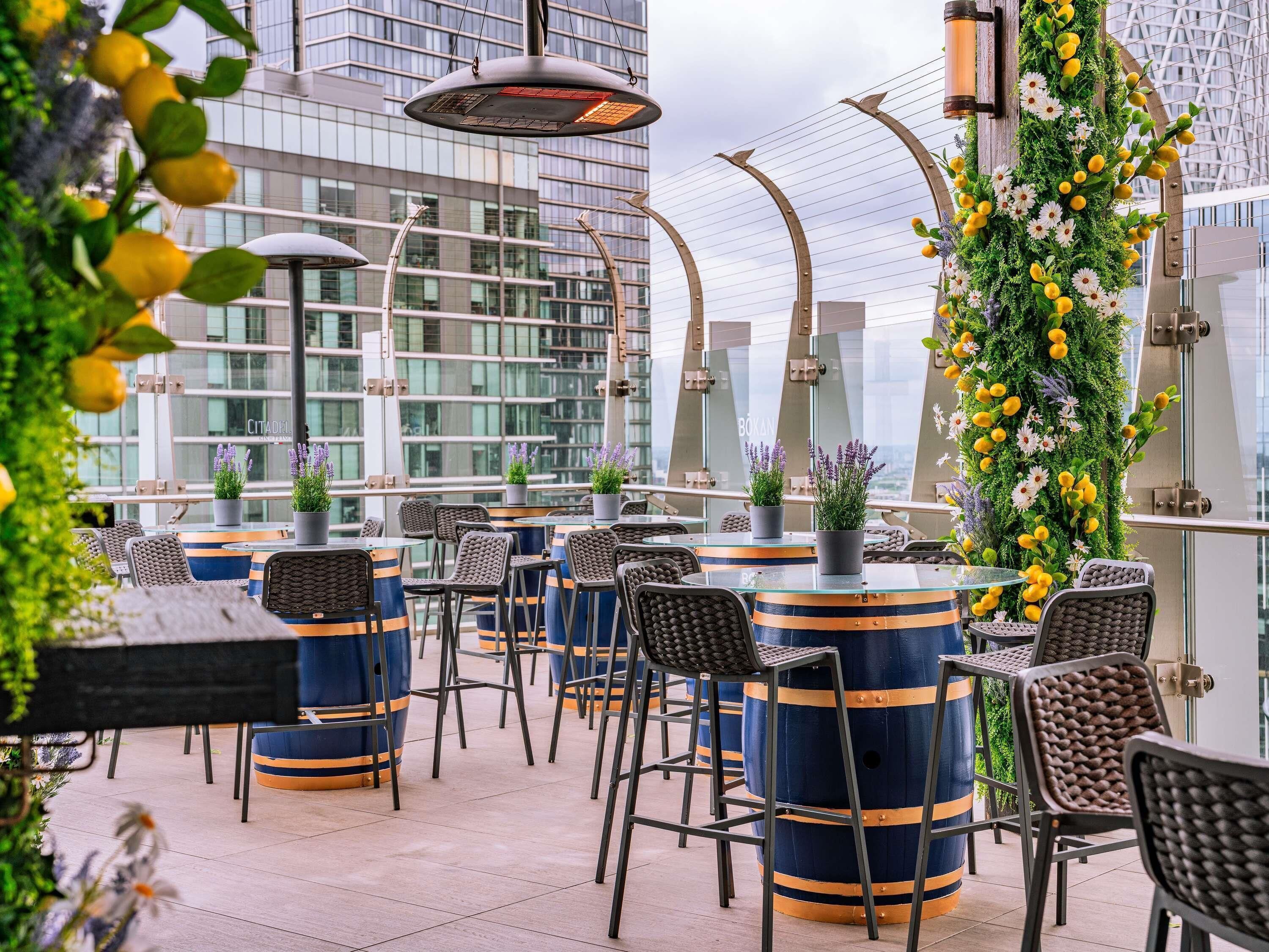 An outdoor seating area with round tables and chairs, potted plants, and a decorative wall with flowers.