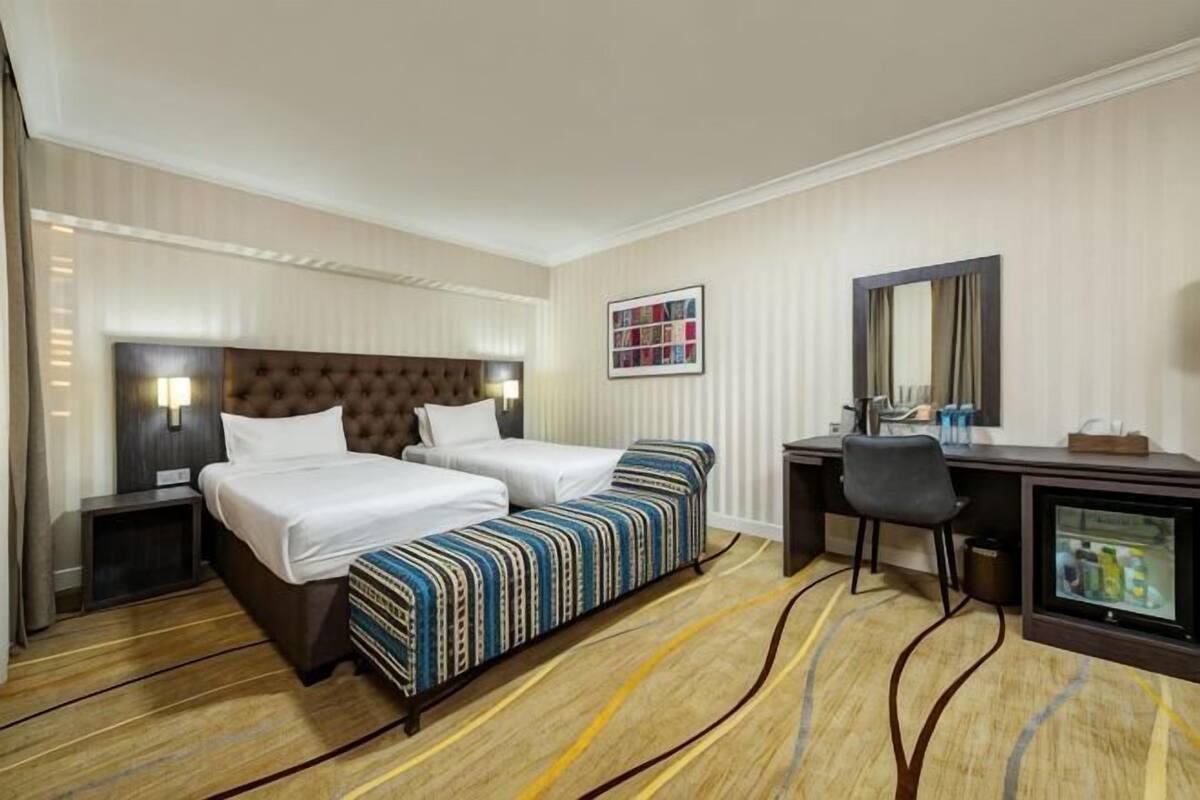 A hotel room with two beds, a desk, a chair, a TV, and a bathroom.