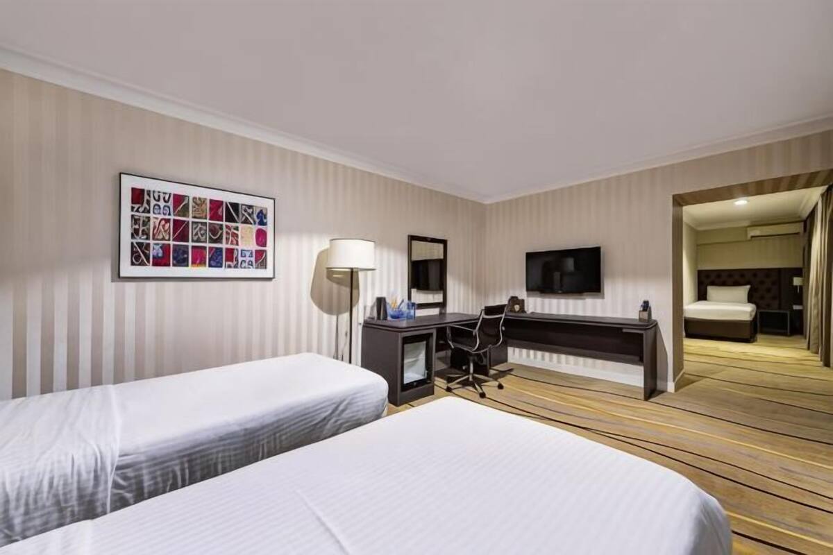 A hotel room with two beds, a desk, a chair, a TV, and a mirror.