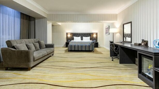A hotel room with a bed, a sofa, a desk, and a television. - Shymkent Grand Hotel (Shymkent)