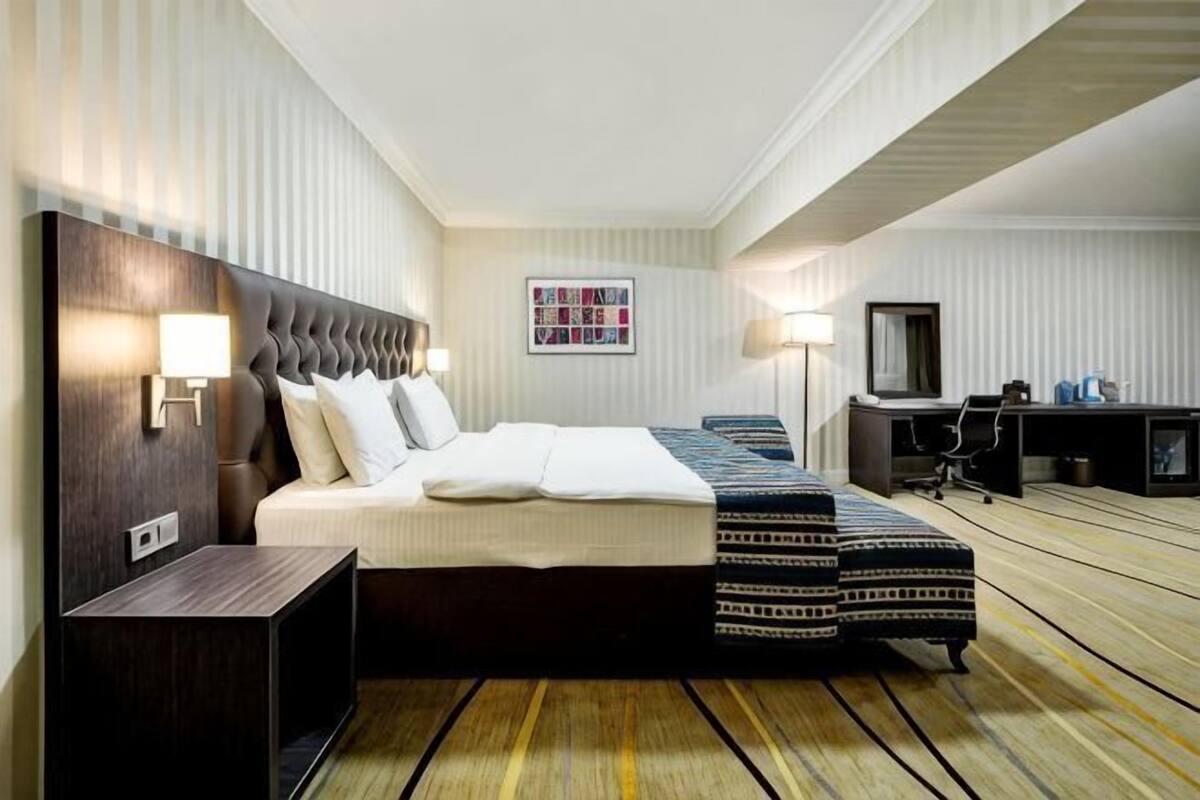 A hotel room with a large bed, a desk, a chair, and a television.