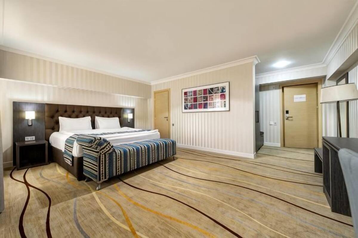 A hotel room with a bed, bedside tables, a flat-screen TV, a framed picture on the wall, and a carpeted floor.