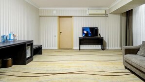 A hotel room with a television, a sofa, a carpet, and a door. - Shymkent Grand Hotel (Shymkent)