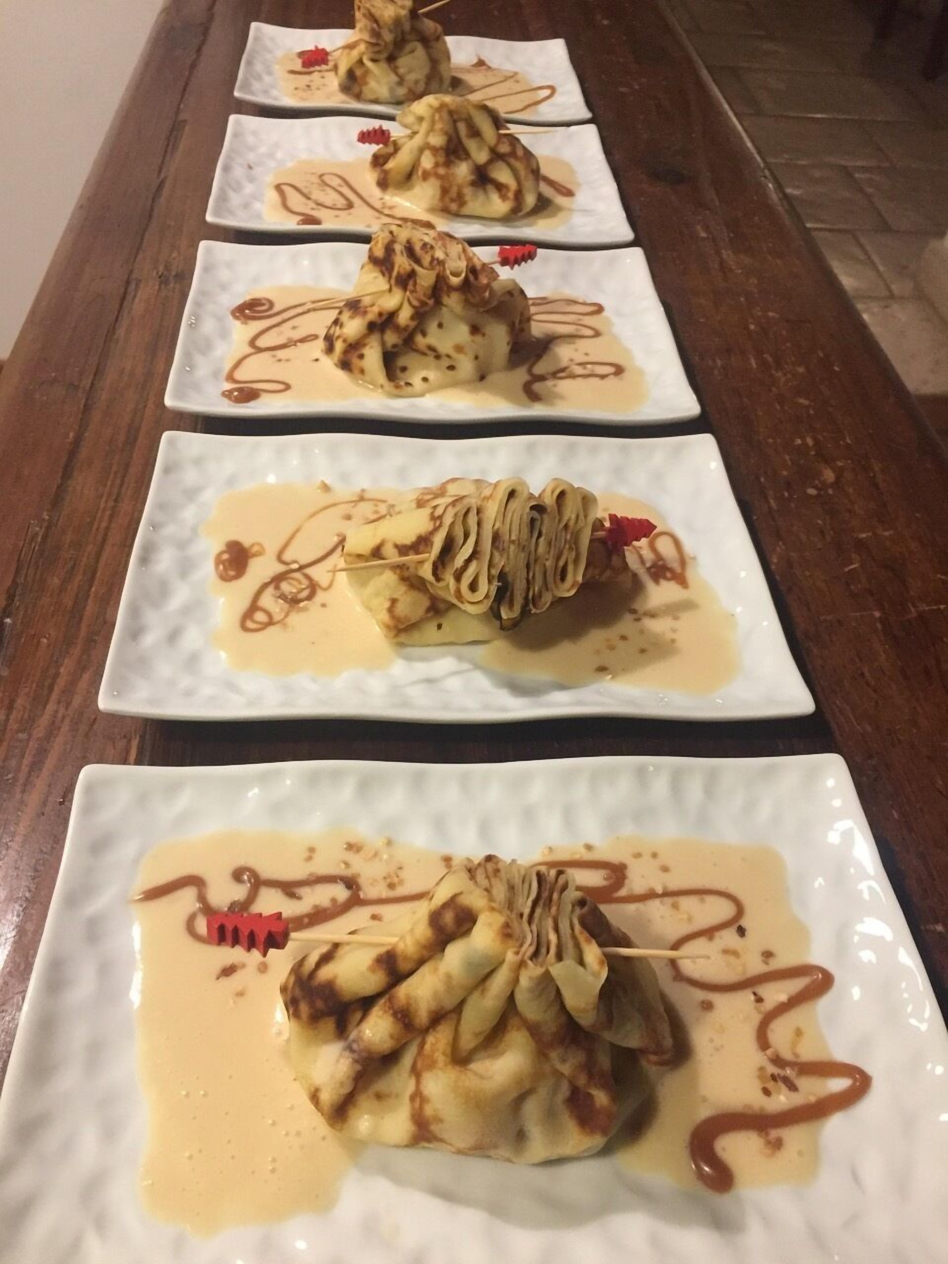 Une rangée d’assiettes carrées présente un dessert composé de crêpes roulées, nappées de sauce et décorées d’une fleur rouge.