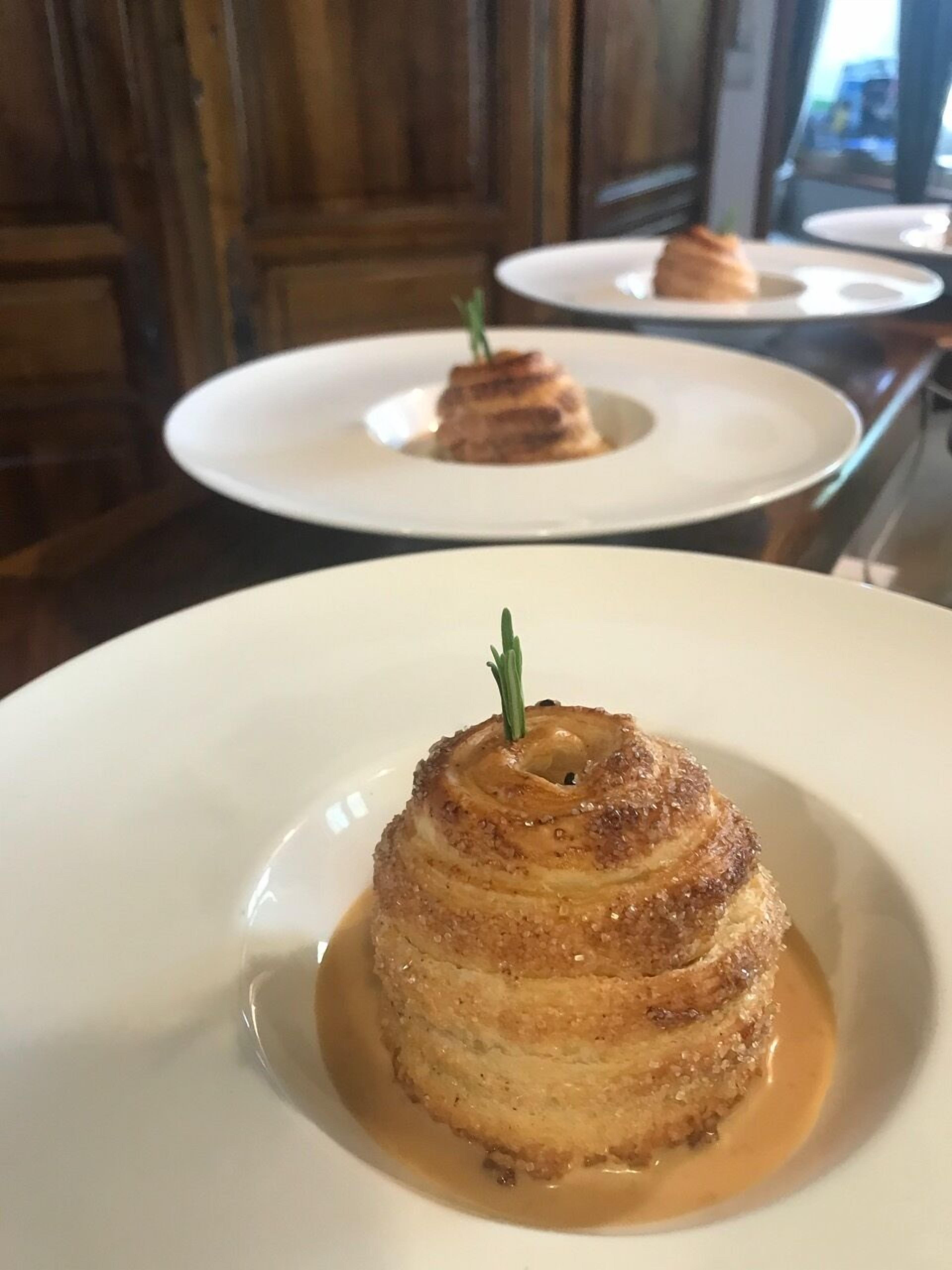 A dessert on a white plate with caramel sauce and a sprig of rosemary.