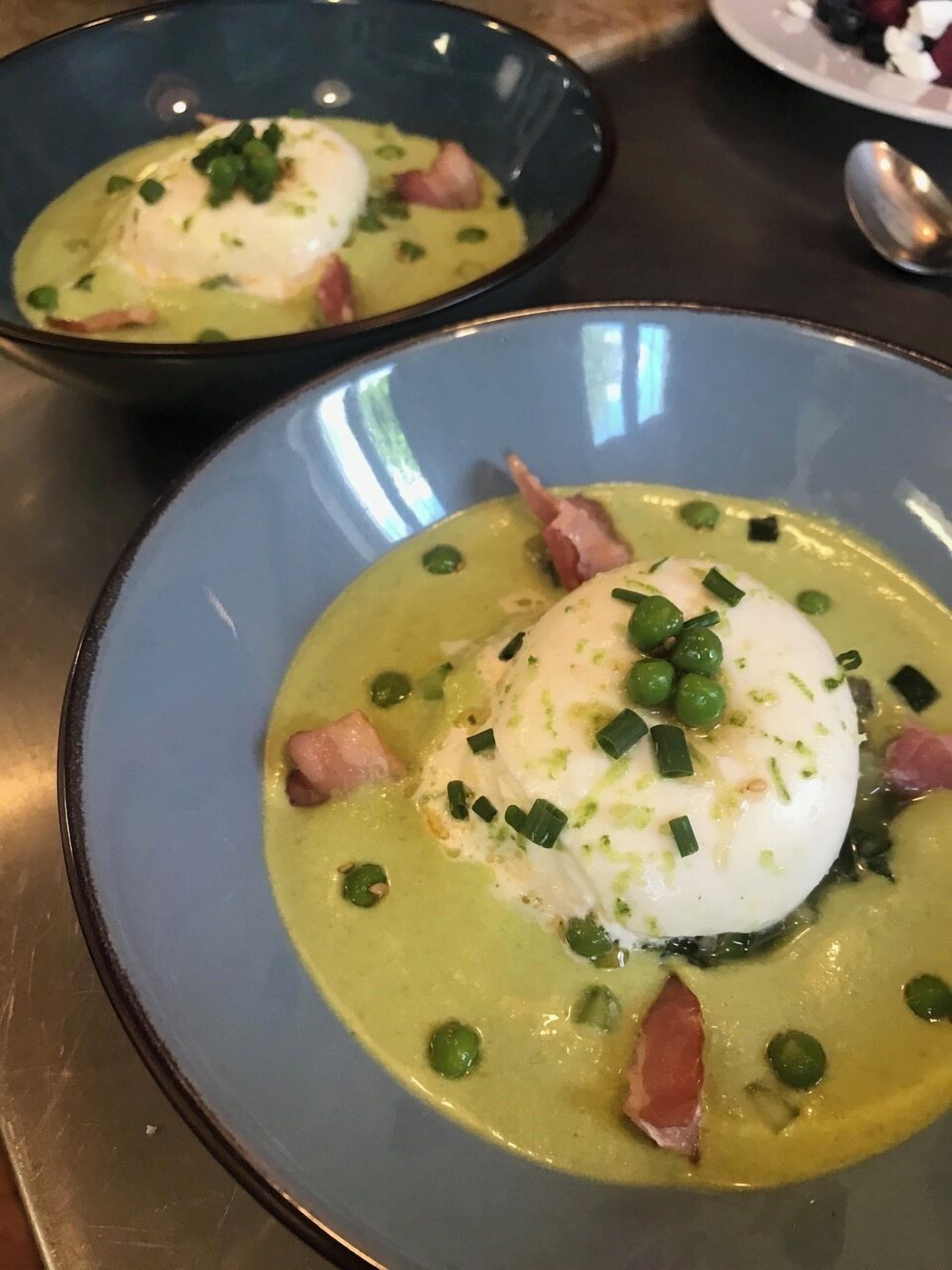 Two bowls of soup with poached eggs, peas, and bacon garnished with chives.