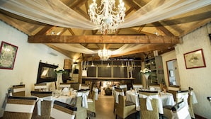 Un restaurante con techos altos de madera, candelabros, sillas de mimbre y manteles blancos.
