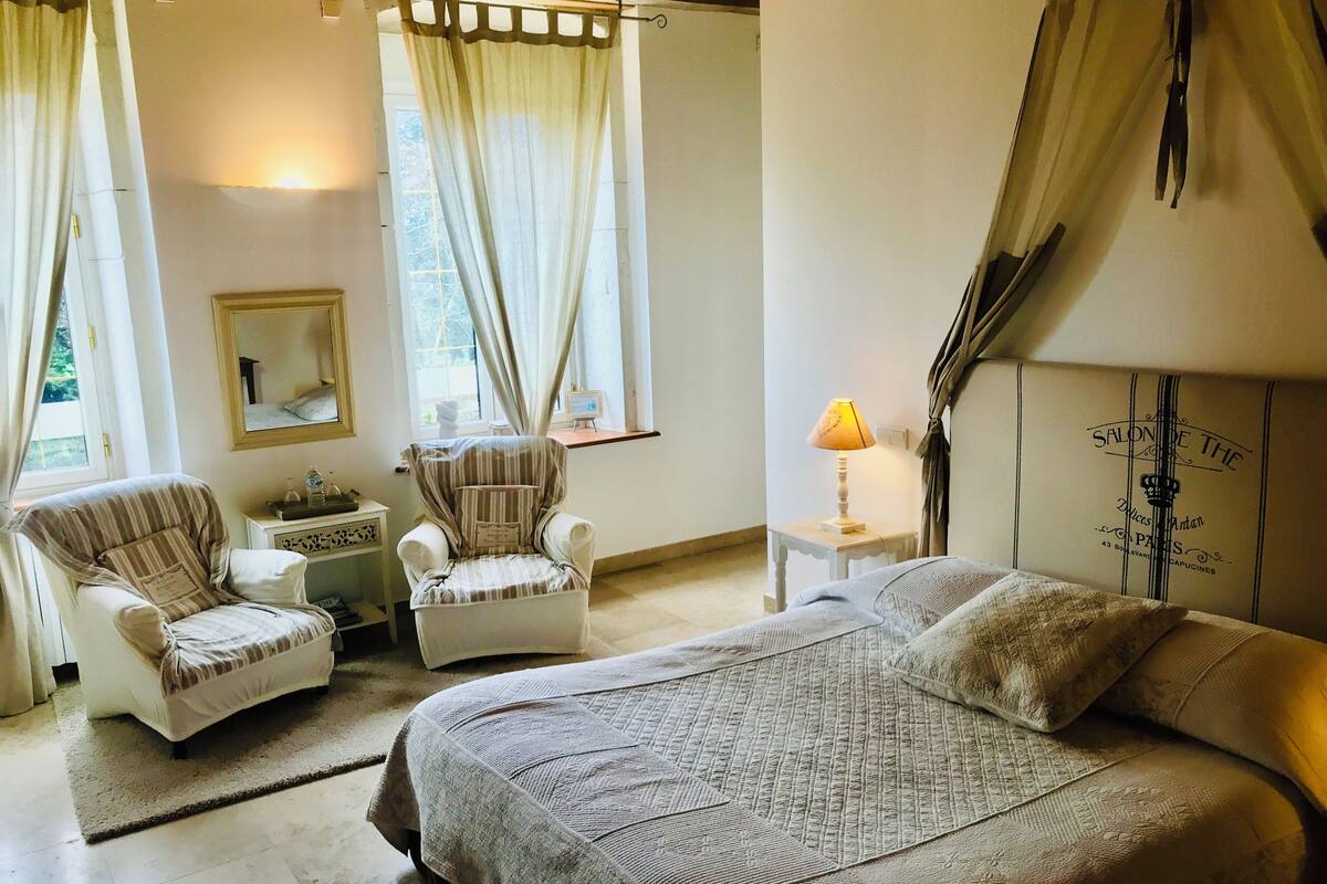 Une chambre à coucher avec un grand lit, deux fauteuils, une petite table et une lampe.