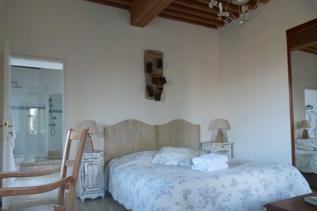Une chambre à coucher avec un lit en bois, deux tables de chevet avec des lampes, une chaise et un miroir.