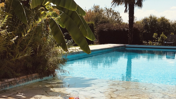 Una piscina cristalina con una copa de vino tinto y gafas de sol al borde.