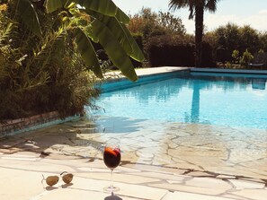 A clear swimming pool with a glass of red wine and sunglasses on the poolside.