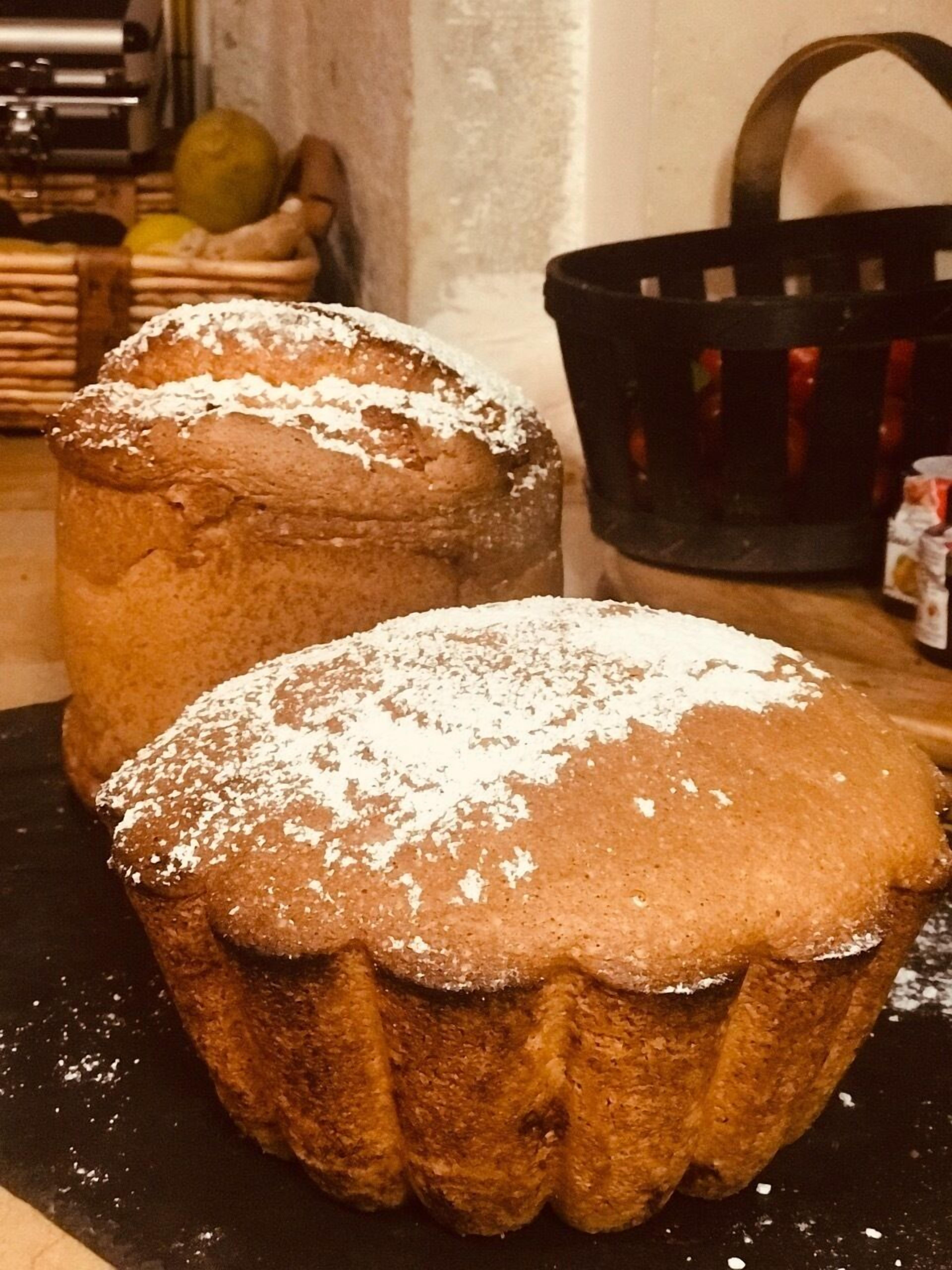 Two round, brown baked goods with powdered sugar on top, placed on a dark surface.