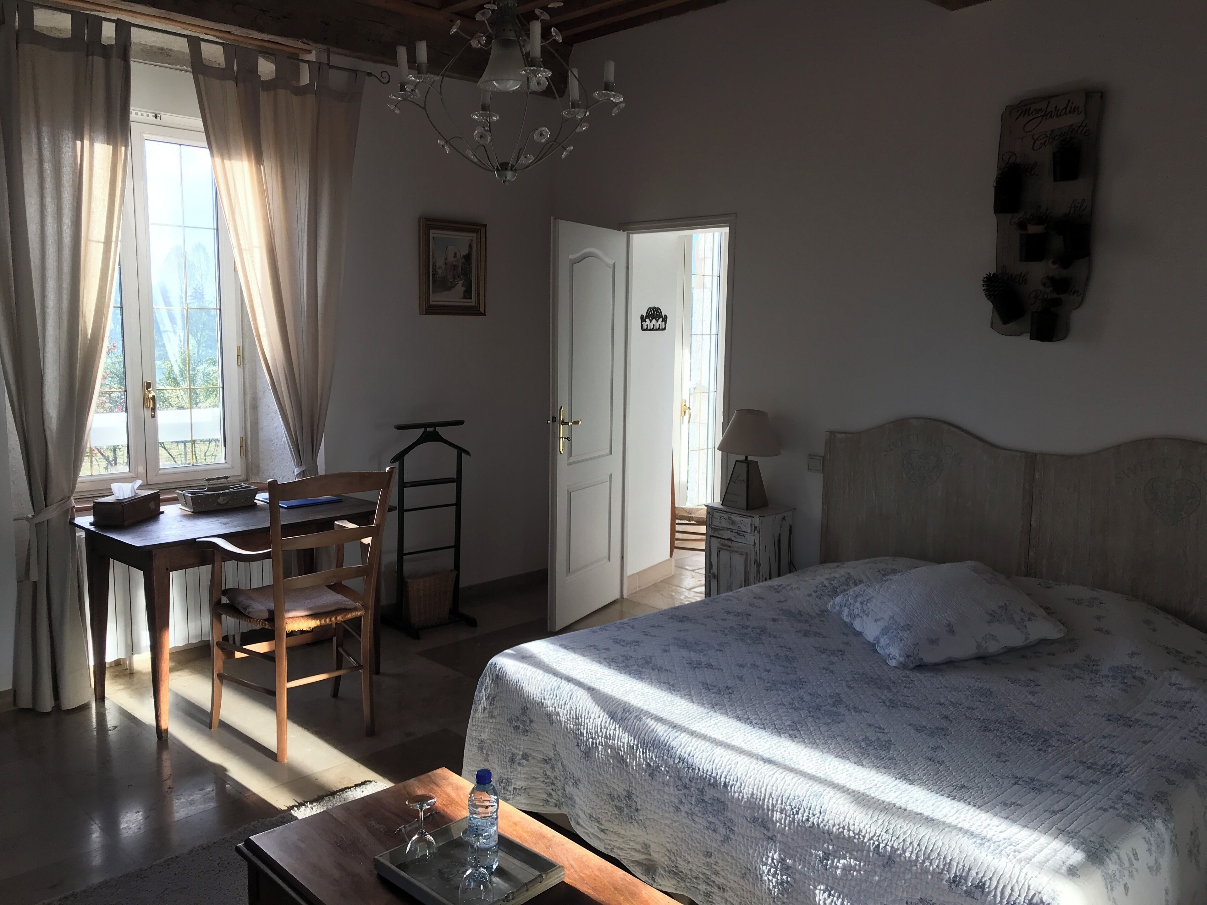 A bedroom with a bed, a desk, and a chair. There is a chandelier above the desk.