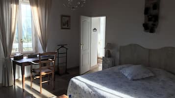 A bedroom with a bed, a desk, and a chair. There is a chandelier above the desk.