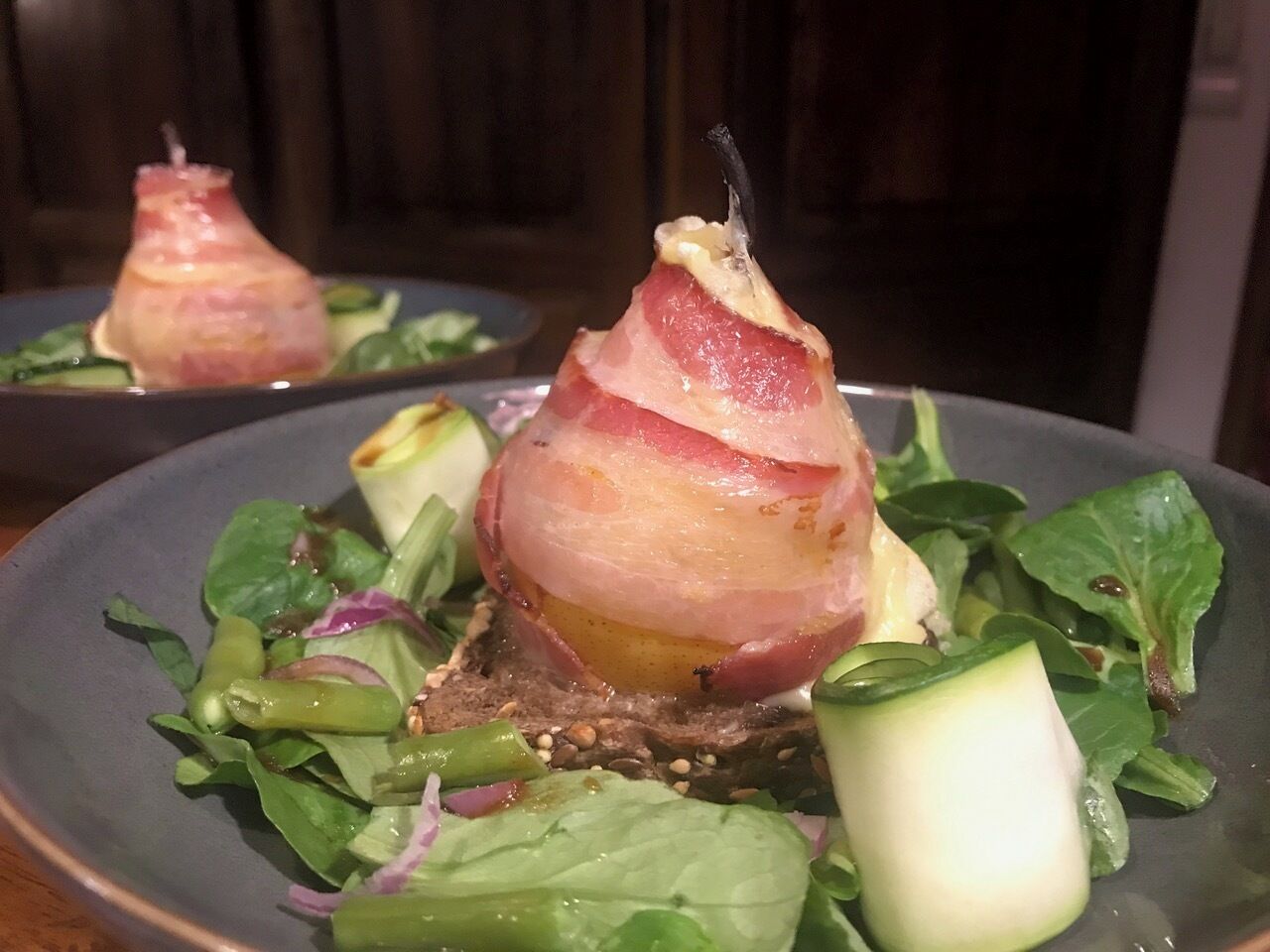 A plate with a salad, including greens, a pear, and a piece of meat wrapped in bacon.