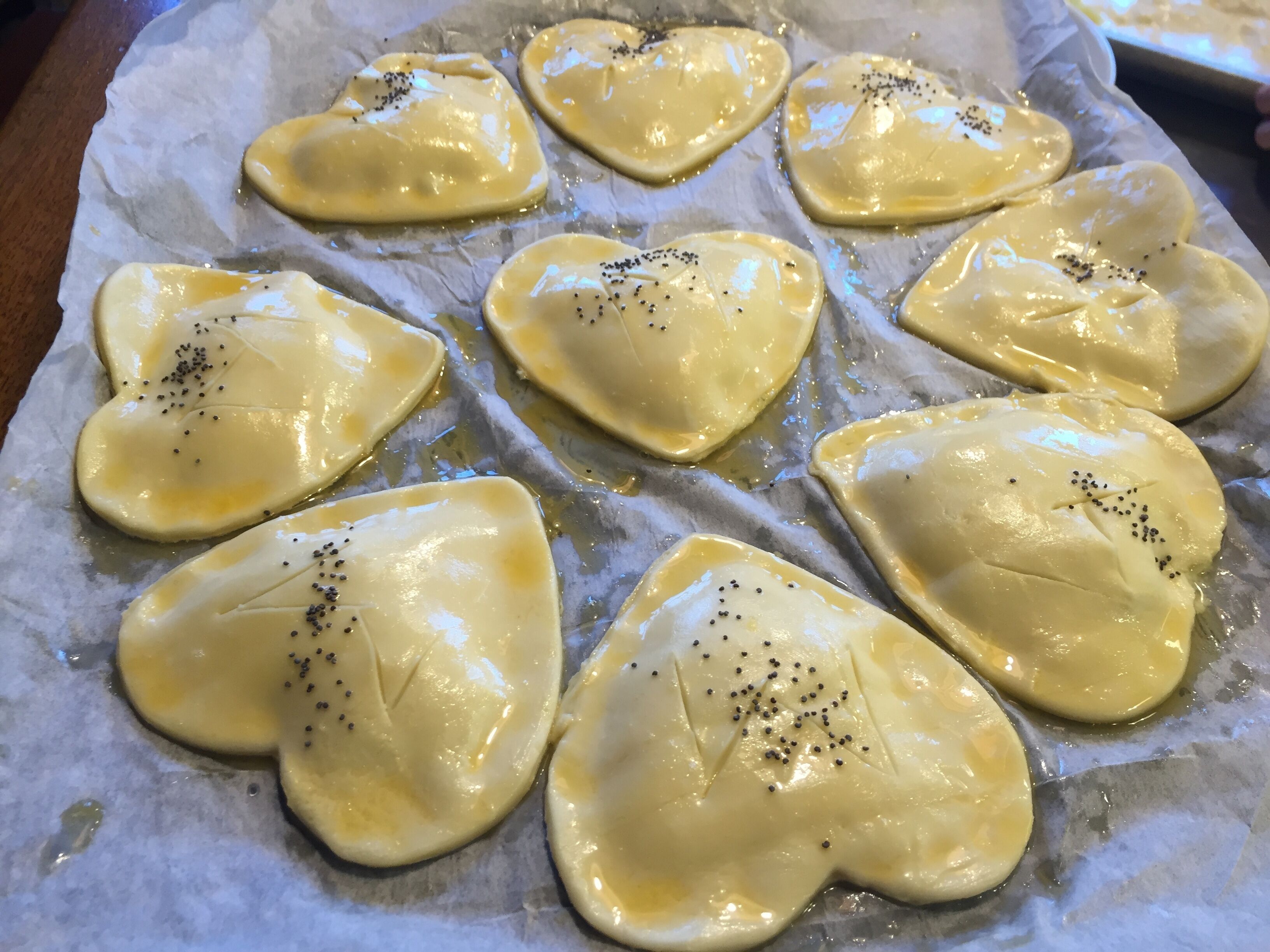 A tray of heart-shaped pastries with black seeds on parchment paper.