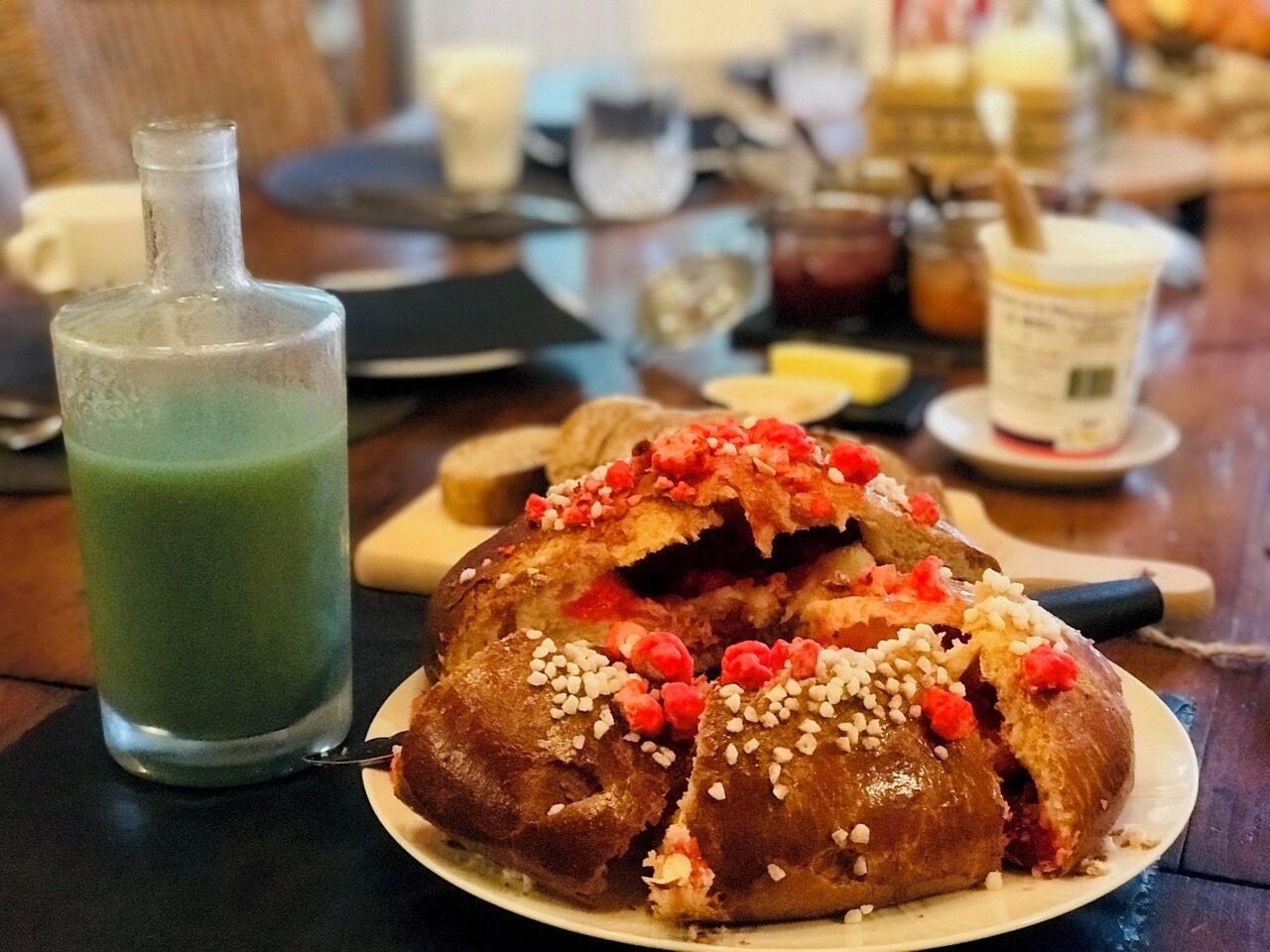 Ein Tisch mit einem grünen Getränk, einem Gebäck mit roten und weißen Toppings sowie verschiedenen Beilagen.