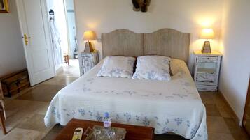 Une chambre à coucher bien rangée, avec un grand lit, deux tables de chevet avec des lampes, une petite table en bois et une autre table sur laquelle se trouvent une bouteille et des verres.