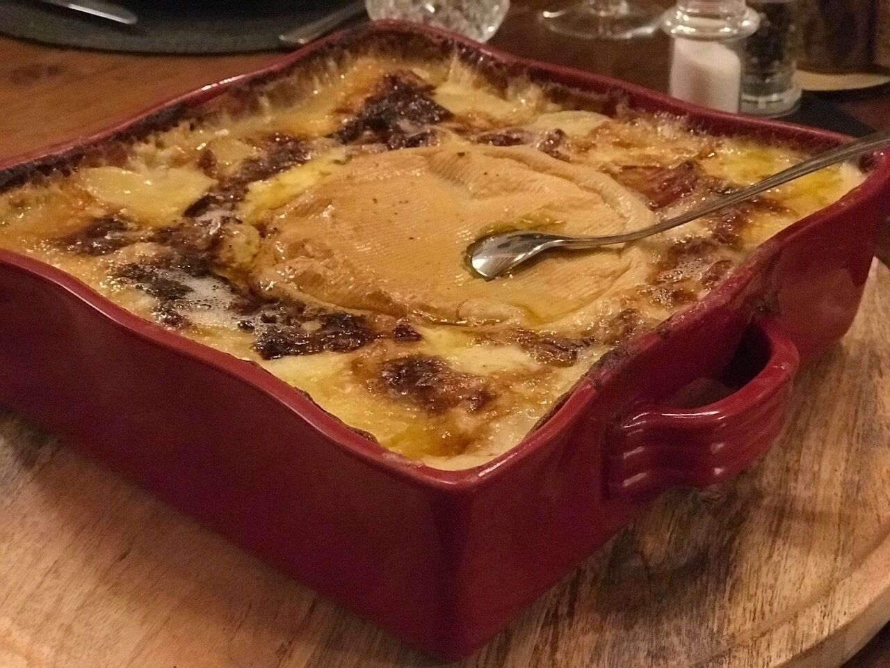 A red baking dish with a golden-brown top, likely containing a baked dish, on a wooden surface.