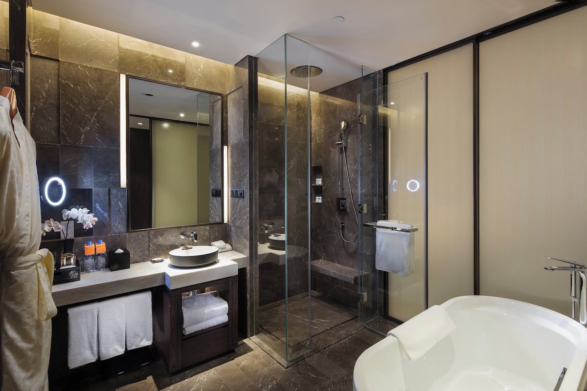 Une salle de bain moderne dotée d’une douche à parois de verre, d’une baignoire sur pieds et d’un meuble-lavabo agrémenté d’un grand miroir et d’un pare-baignoire en marbre.