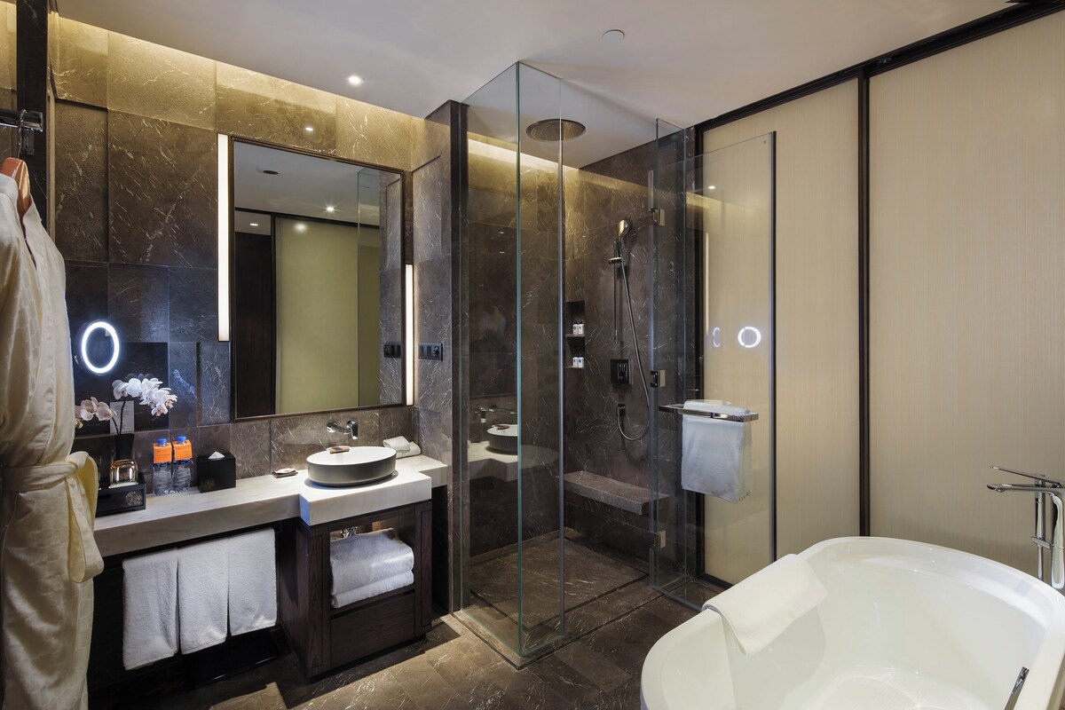 A modern bathroom with a glass-enclosed shower, a freestanding bathtub, and a vanity with a large mirror and marble backsplash.