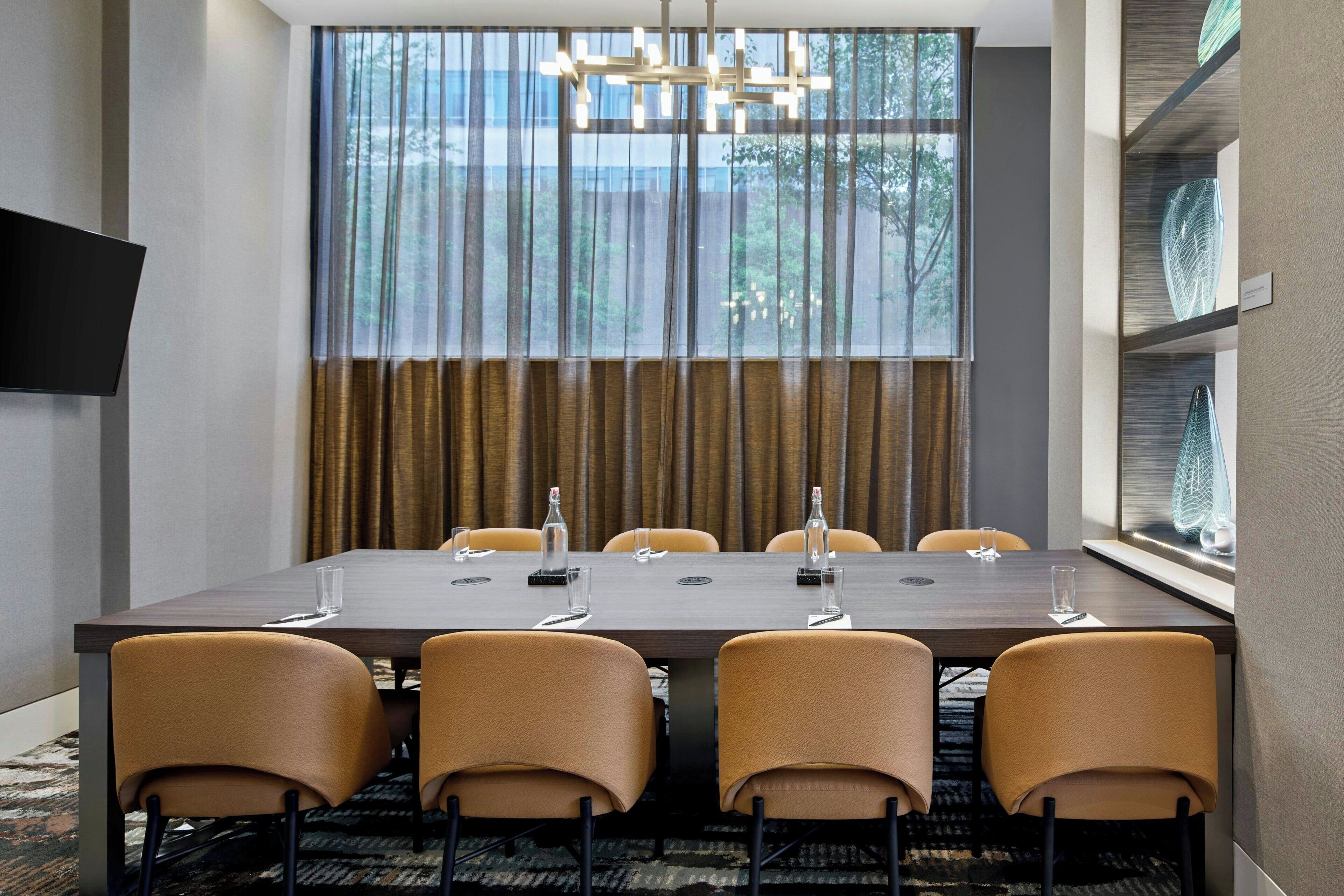 Une salle de conférence dotée d’une grande table, de six chaises, d’un lustre et offrant une vue sur les arbres par la fenêtre.