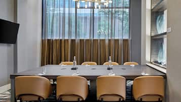 Ein Konferenzraum mit einem großen Tisch, sechs Stühlen, einer Kronleuchter und Blick auf Bäume durch das Fenster.